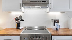 A modern kitchen with a stainless steel stove, a built-in oven, and a range hood above the stove. There is a wooden countertop and a set of kitchen utensils on the left.