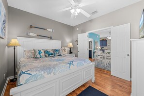 Une chambre à coucher avec un lit, des lampes de chevet, un ventilateur de plafond et une vue sur la cuisine adjacente.