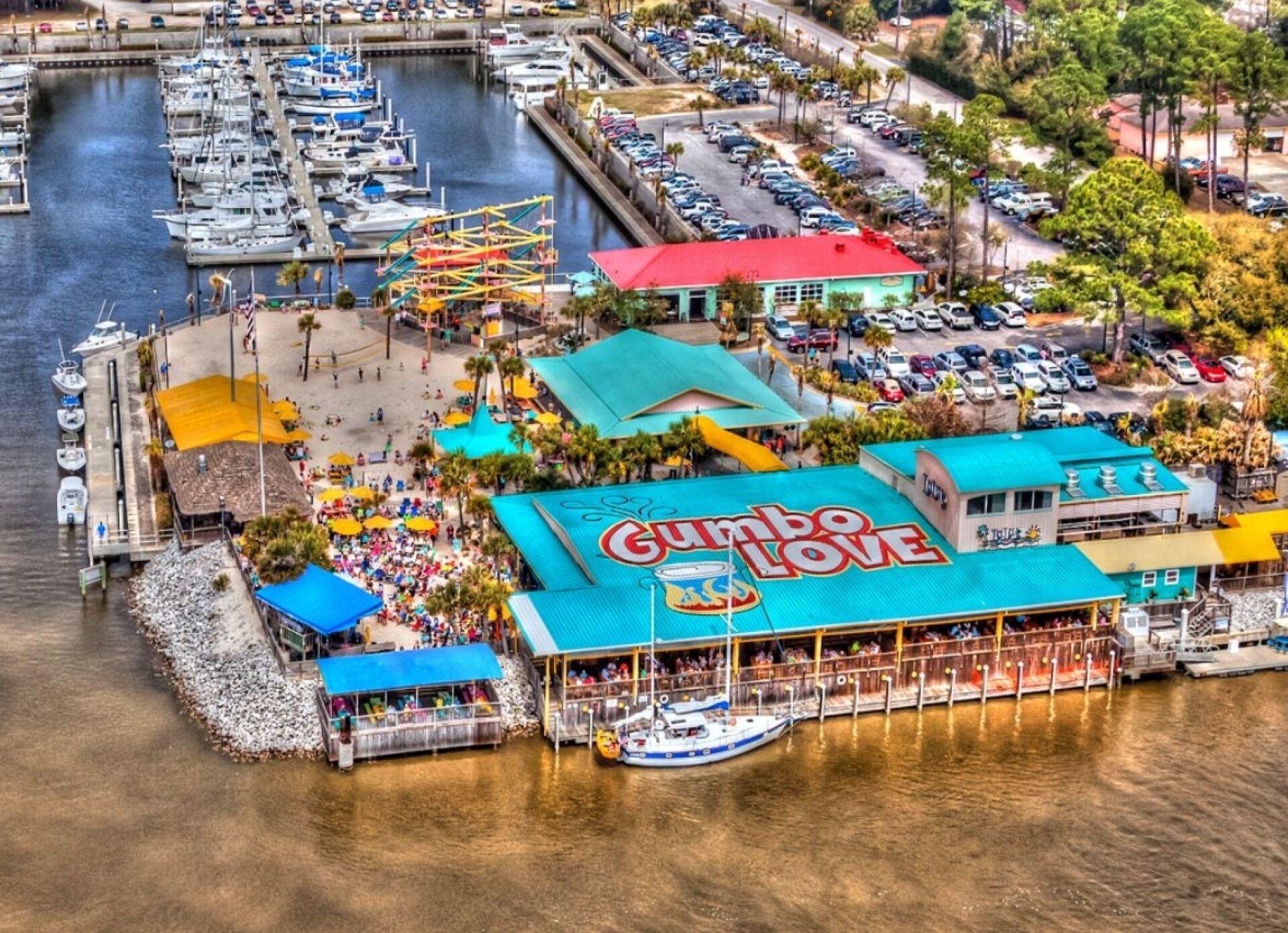 A waterfront restaurant with a prominent sign, a dock with boats, and a parking area.