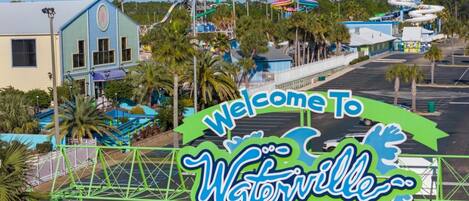 A welcome sign for Waterwell with a clear view of the surrounding area including buildings and palm trees.
