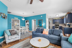 Un salon moderne avec un canapé bleu, une table basse ronde et un coin repas doté de meubles blancs.