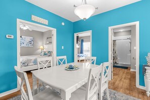 A bright blue room with a white dining table, chairs, and a ceiling fan.