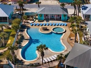 A resort with a large swimming pool, lounge chairs, and palm trees.