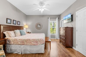 A bedroom with a bed, bedside tables, a dresser, a ceiling fan, a wall clock, and a window with curtains.