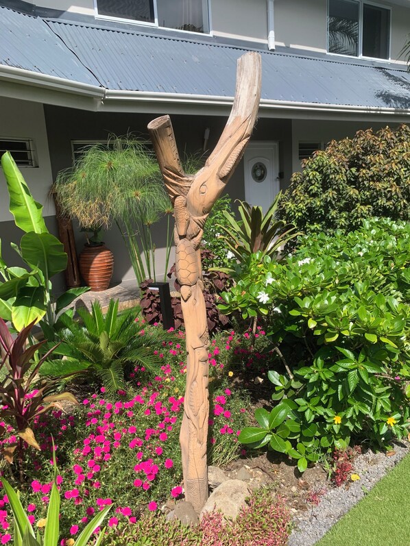 Una escultura de madera en un jardín con diversas plantas y flores.