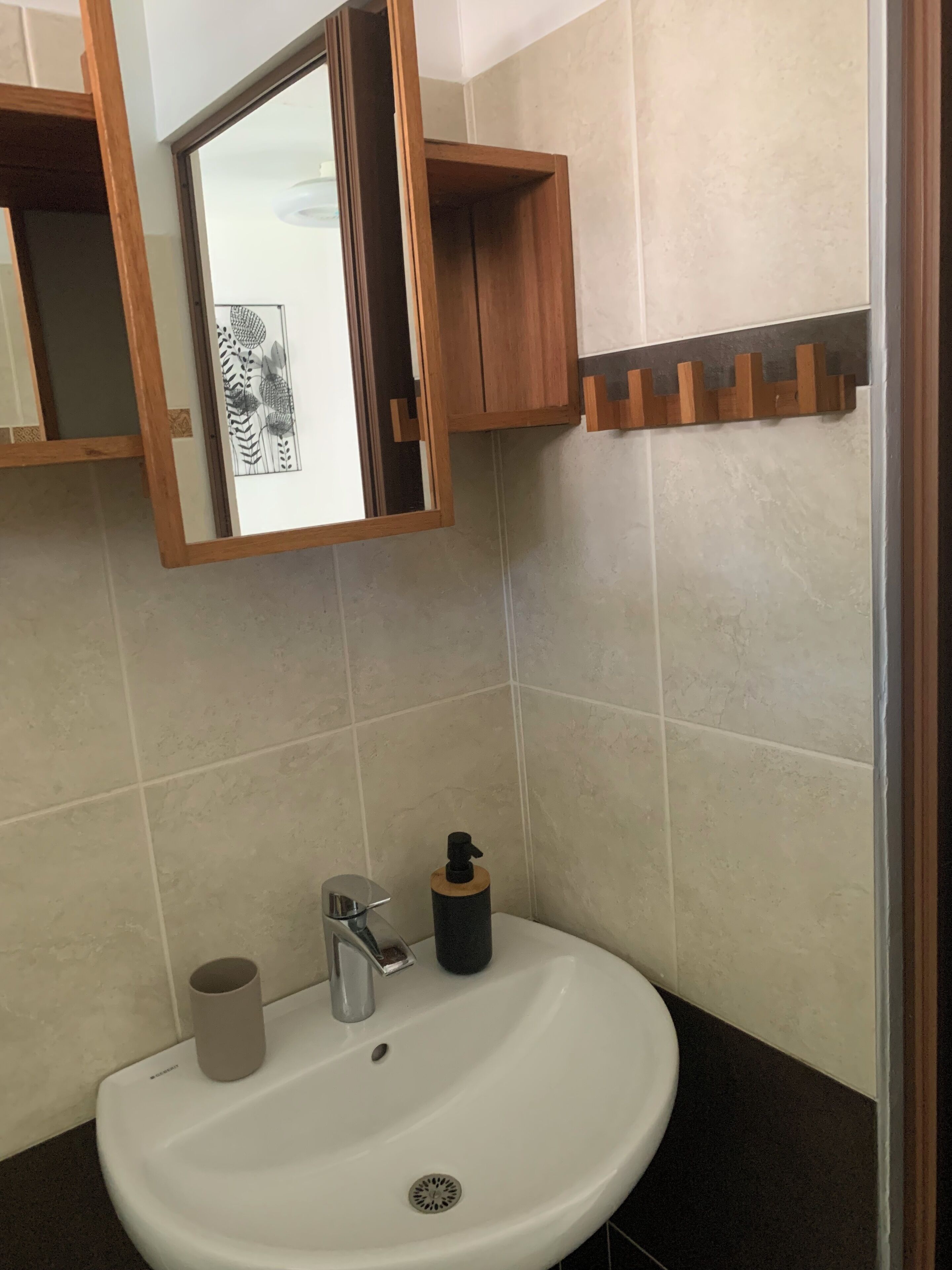 Un baño con un lavamanos blanco, un espejo, un armario de madera para medicamentos y un perchero para toallas.