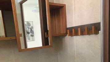 Un baño con un lavamanos blanco, un espejo, un armario de madera para medicamentos y un perchero para toallas.