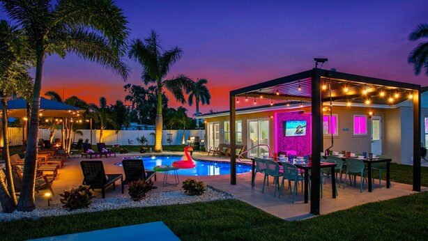 Ein Poolbereich mit Liegestühlen, einem Flamingo-Schwimmpfad und einer überdachten Terrasse mit Lichterketten.