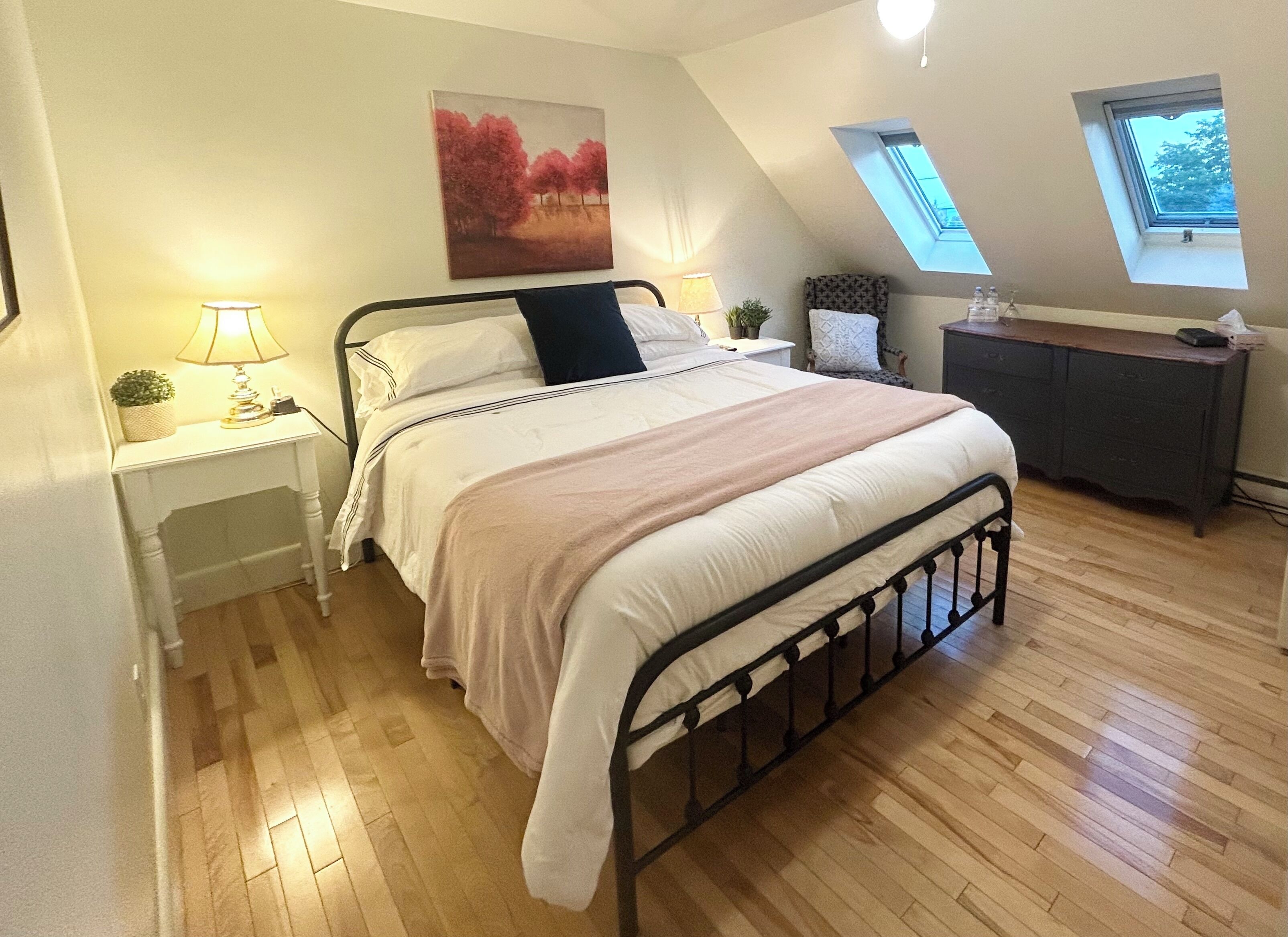 Een slaapkamer met een bed, nachtkastjes, een bureau, een raam en een dakraam.
