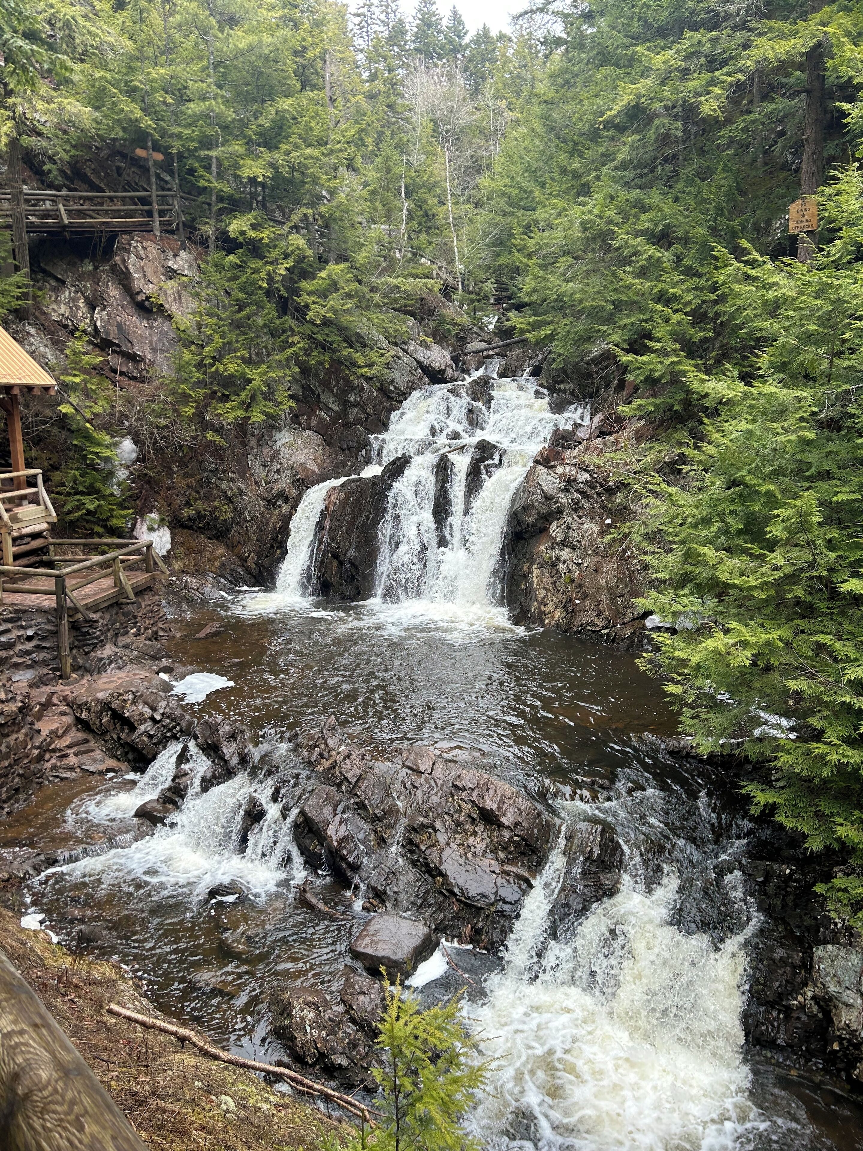 A wooden viewing platform overlooking a cascading waterfall surrounded by dense forest.