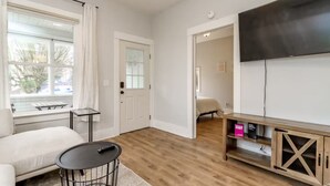 A modern living room with a sofa, a round coffee table, a TV mounted on the wall, and a wooden cabinet with a glass door.