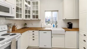 A modern kitchen with white cabinets, a built-in microwave, a dishwasher, and a wooden countertop.