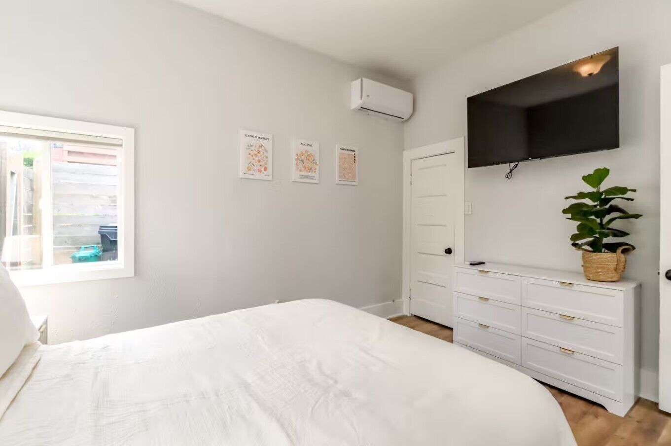 A bedroom with a bed, a dresser, a TV mounted on the wall, and a window with blinds.