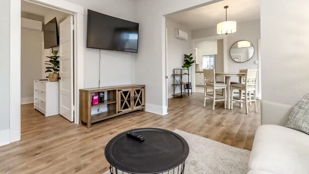 A modern living room with a flat-screen TV, a coffee table, and a dining area with a chandelier.