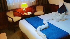 Une chambre d’hôtel avec un grand lit, un bureau avec une lampe, une chaise et une fenêtre avec des rideaux.