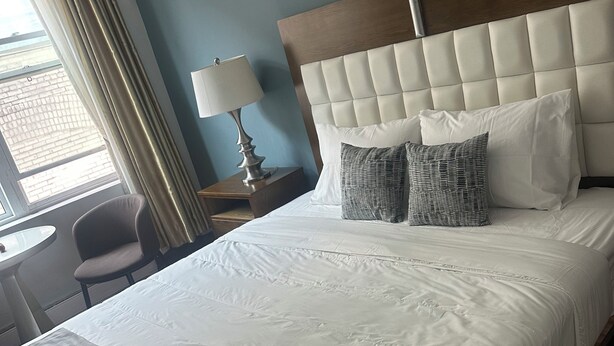A neatly made bed with a tufted headboard, a bedside lamp, and two pillows. - King bed suite in the heart of downtown, festive atmosphere (Montréal)