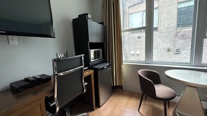 A compact hotel room with a flat-screen TV, a kitchenette, a wooden desk, a chair, and a small table. - King bed suite in the heart of downtown, festive atmosphere (Montréal)