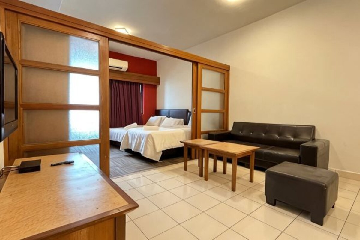 A hotel room with a bed, a sofa, a small table, a TV, and a sliding door.