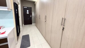 A hallway with a black door at the end, a white counter with a red object on it, and a grey mat on the floor. - Cempaka Apartment By Easy Nap (Kuala Lumpur)