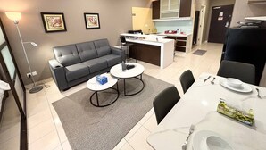 A modern living room with a grey sofa, two coffee tables, and a dining area with a white table set for two. - Cempaka Apartment By Easy Nap (Kuala Lumpur)