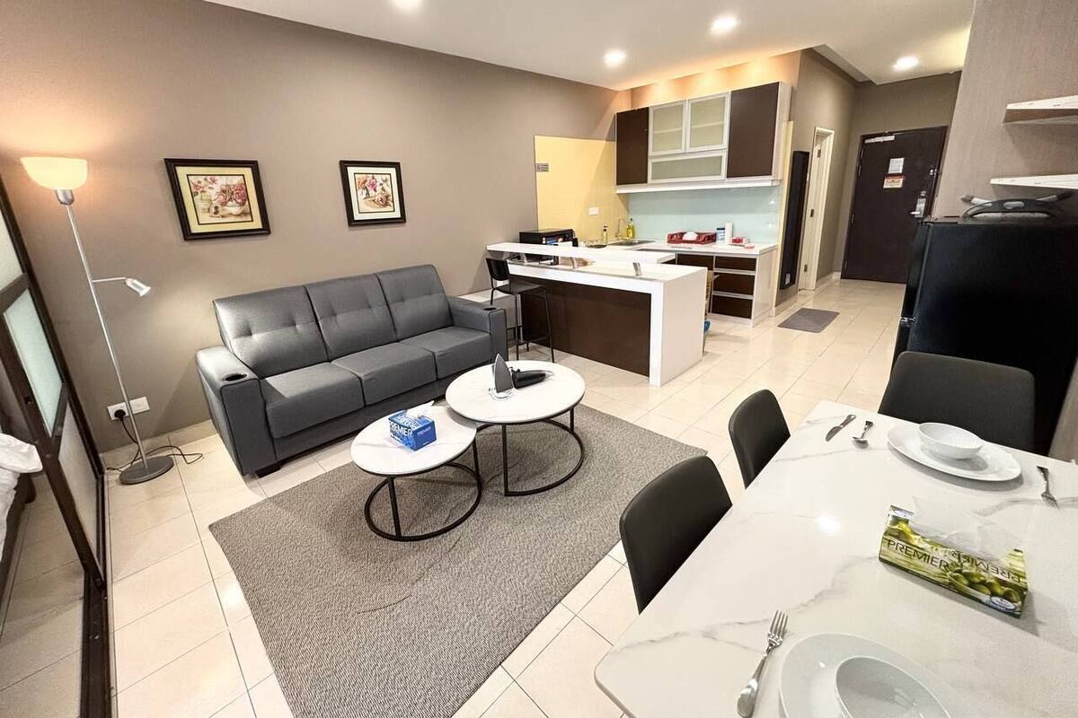 Una sala de estar moderna con un sofá gris, dos mesas de centro y una zona de comedor con una mesa blanca dispuesta para dos personas.