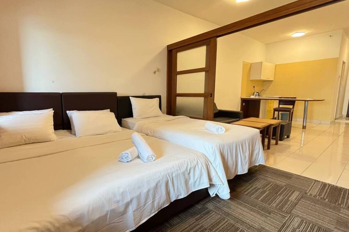 Habitación de hotel con dos camas, una kitchenette pequeña y vista al pasillo.