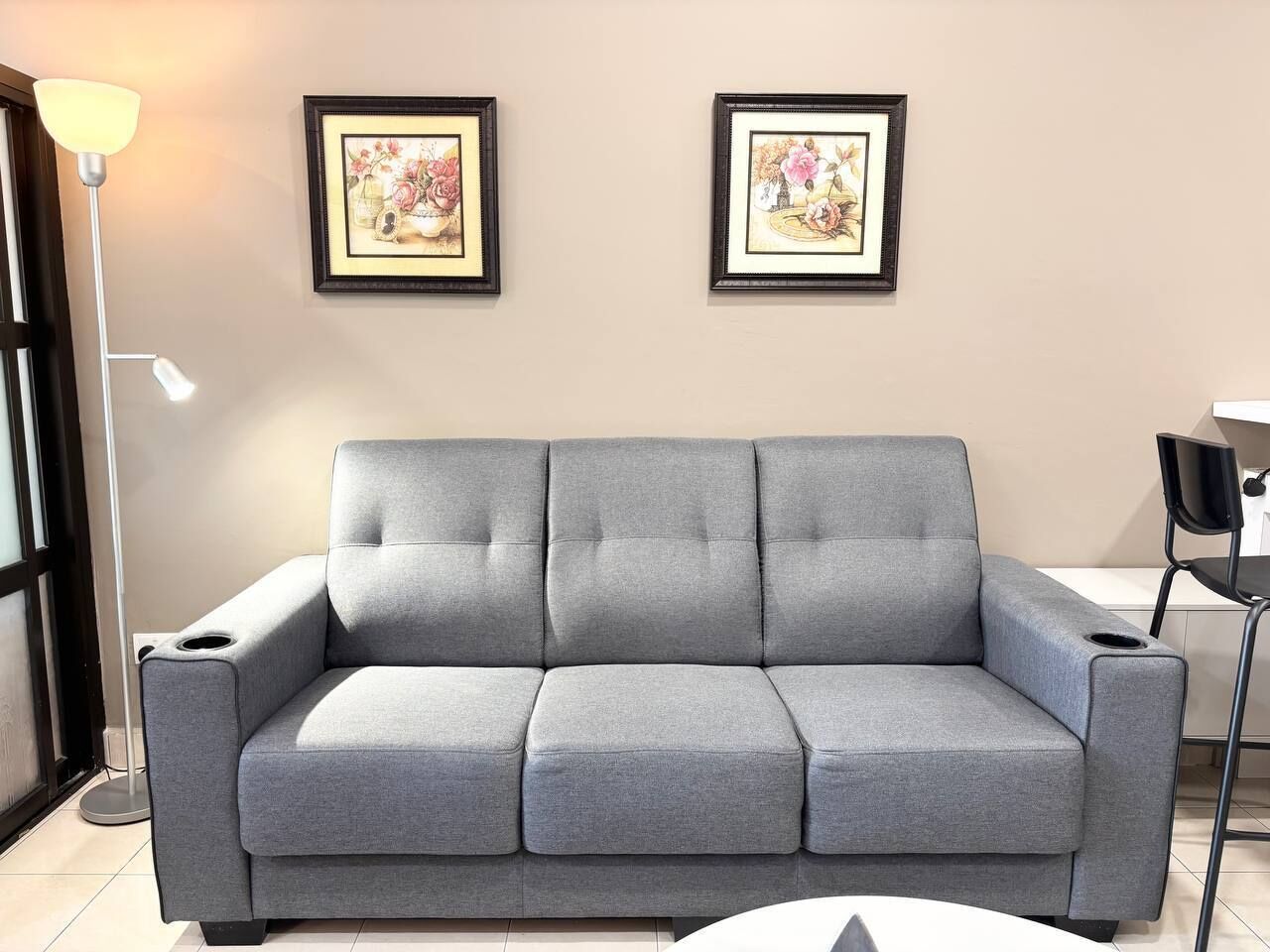 A grey sofa in a room with two framed floral artworks on the wall, a floor lamp, and a chair.