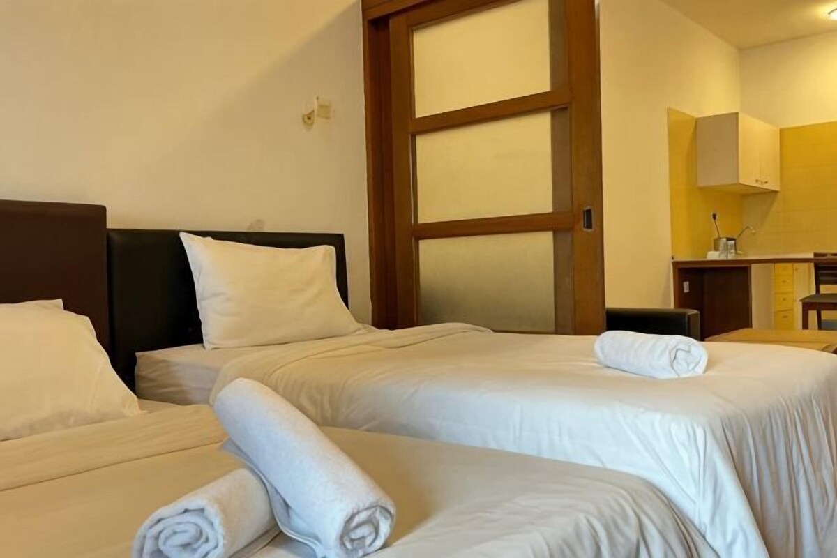 Une chambre d’hôtel avec deux lits, une tête de lit en bois, une grande fenêtre et un coin cuisine.