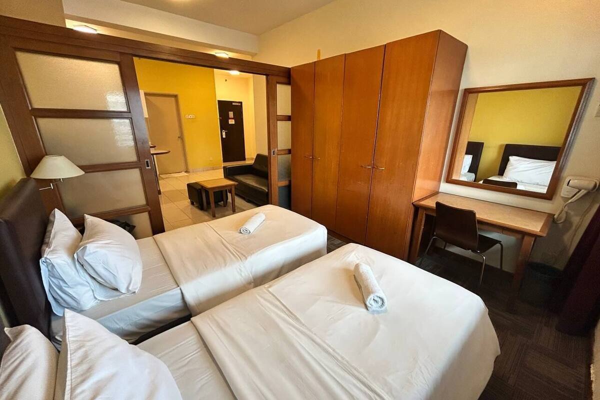 Una habitación de hotel con dos camas, un escritorio, una silla, un armario y un espejo.