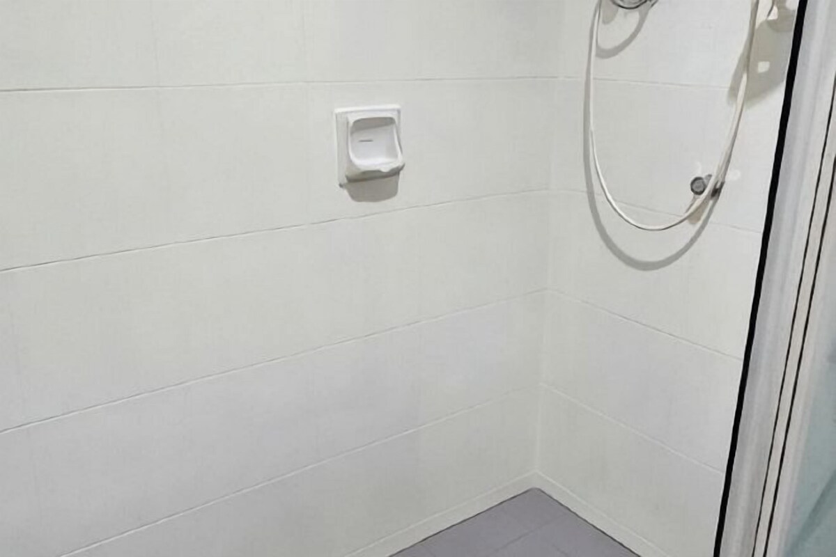 Une douche avec une porte en verre, un mur recouvert de carreaux blancs et un distributeur de savon.