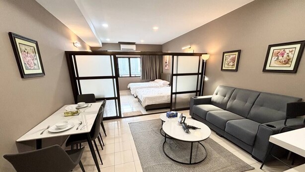 A modern hotel room with a dining area, a sofa, a coffee table, and a bed with a view. - Cempaka Apartment By Easy Nap (Kuala Lumpur)