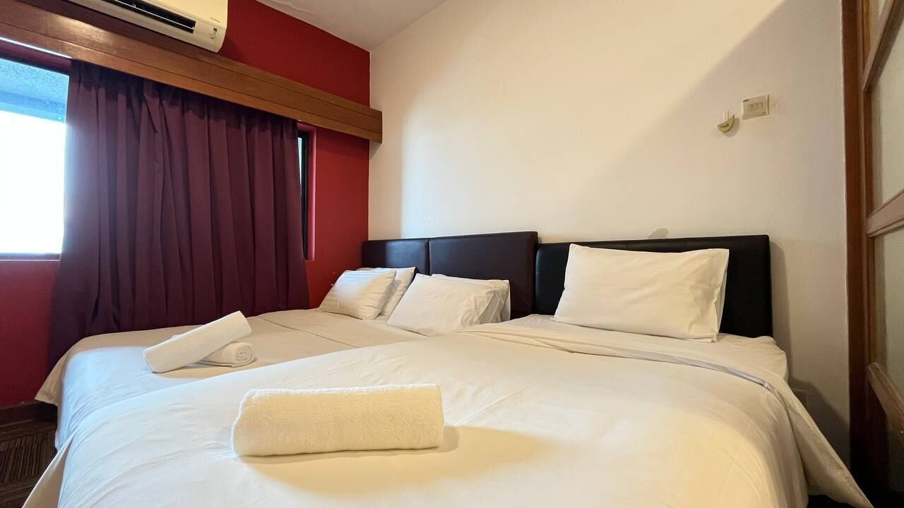 A hotel room with a large bed, a window with curtains, and an air conditioning unit above the bed.
