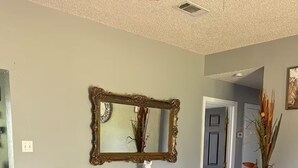 A living room with a light blue armchair, a small side table with a white vase, a large mirror, and a wooden floor. - Skyblue Ranch, Peaceful Getaway with Pool!Pets! (Terrell)