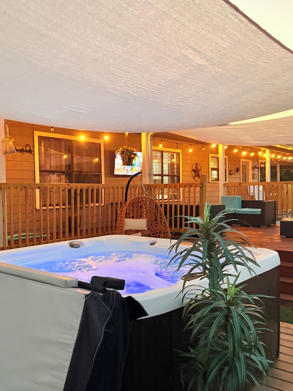 A hot tub with a wooden deck, a wicker chair, and a potted plant.