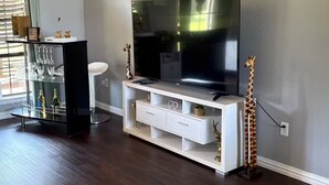 A living room with a flat-screen TV on a white entertainment unit, a glass coffee table, and a giraffe statue. - Skyblue Ranch, Peaceful Getaway with Pool!Pets! (Terrell)