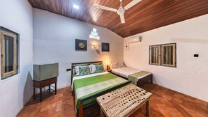 Une chambre à coucher comprenant un lit, une table de chevet, une lampe, une table en bois, un ventilateur de plafond et un téléviseur.