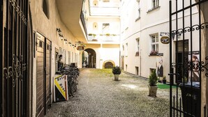 A narrow cobblestone street flanked by buildings with barred gates, a sign for a hair salon, and a statue of a man.