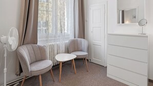 A room with two grey armchairs, a small white table, a white dresser with a mirror, and a radiator.