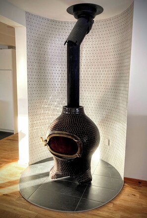 A compact wood-burning stove sits atop a circular platform on a light-colored wooden floor.
