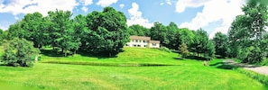 Situated on a grassy hill, this two-story building offers a serene escape amidst lush trees and a clear sky.