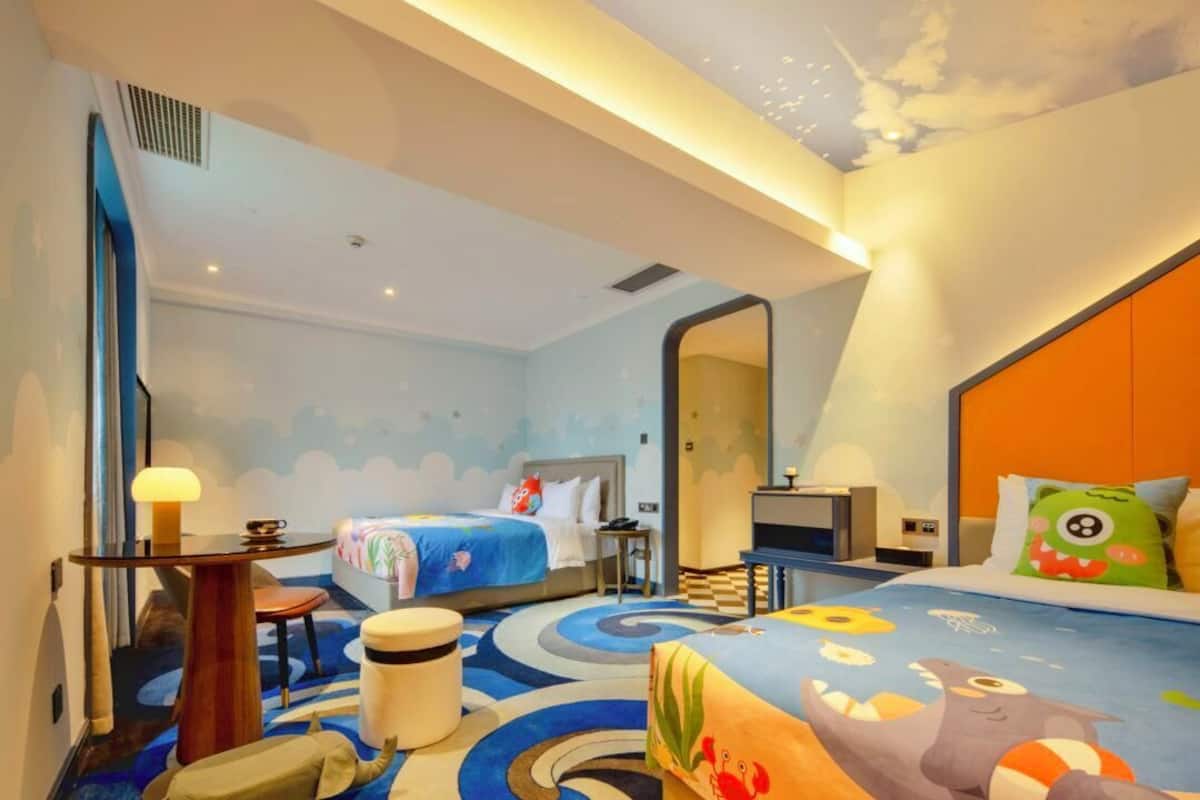 Ein Hotelzimmer mit zwei Betten, einem Schreibtisch, einem Stuhl, einer Lampe und einem großen Spiegel.