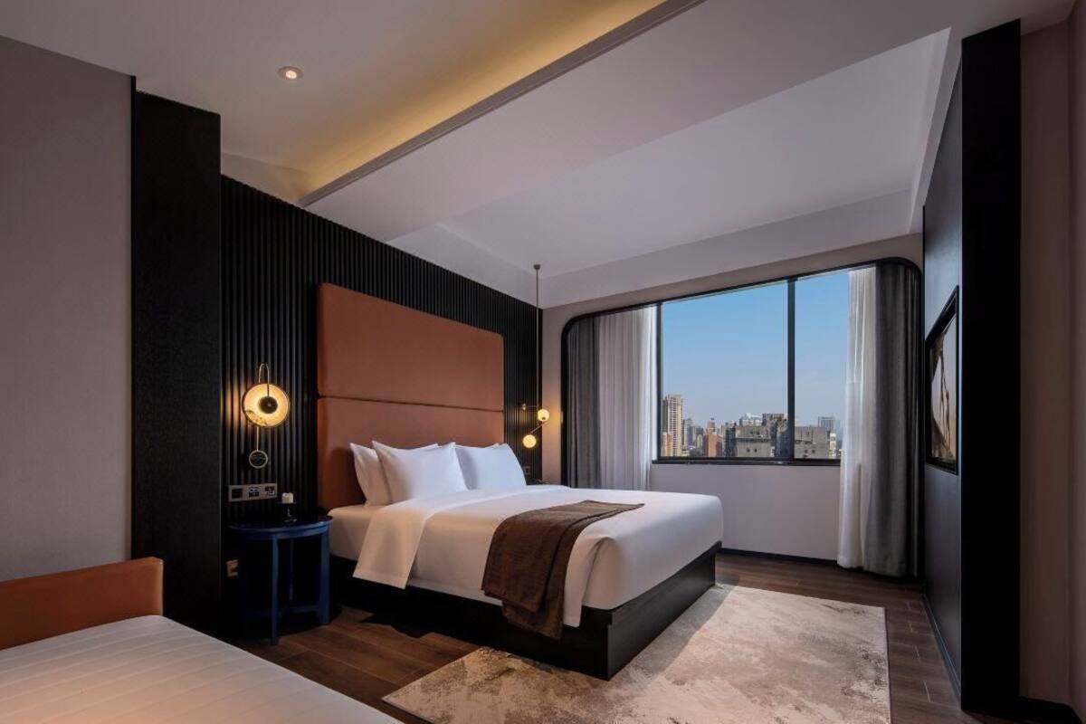 Ein modernes Hotelzimmer mit einem großen Bett, einem Nachttisch, einem Schreibtisch und Blick auf die Stadt.