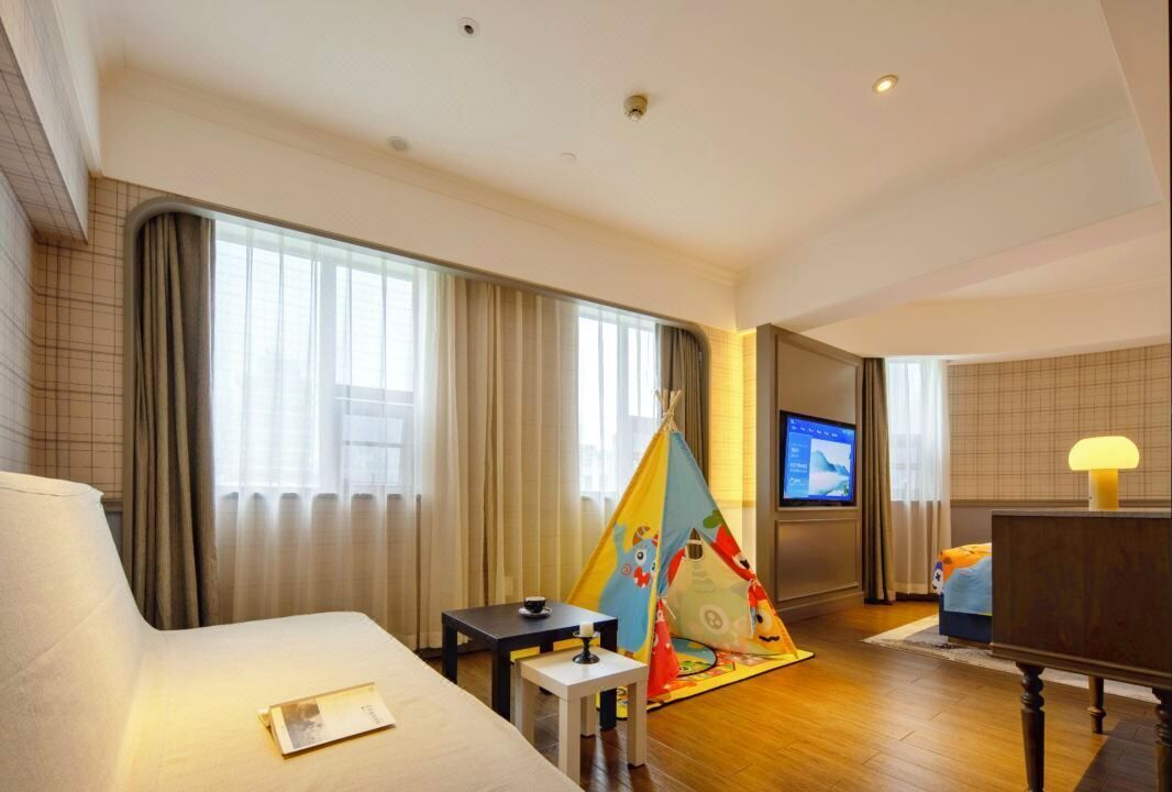 A hotel room with a bed, a small table, a TV, and a colorful play tent.