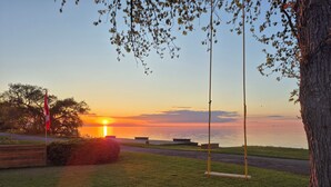 A sunset view over a calm body of water with a flag, a swing set, and a grassy area. - The Marylin Lakehouse (Private Long Dock & Boat Ramp) (Lincoln)