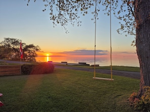 A sunset view over a calm body of water with a flag, a swing set, and a grassy area.