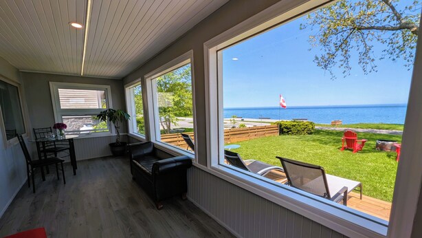 A room with a large window overlooking a grassy area with a flag, a view of the sea, and a dining area with chairs and a table. - The Marylin Lakehouse (Private Long Dock & Boat Ramp) (Lincoln)