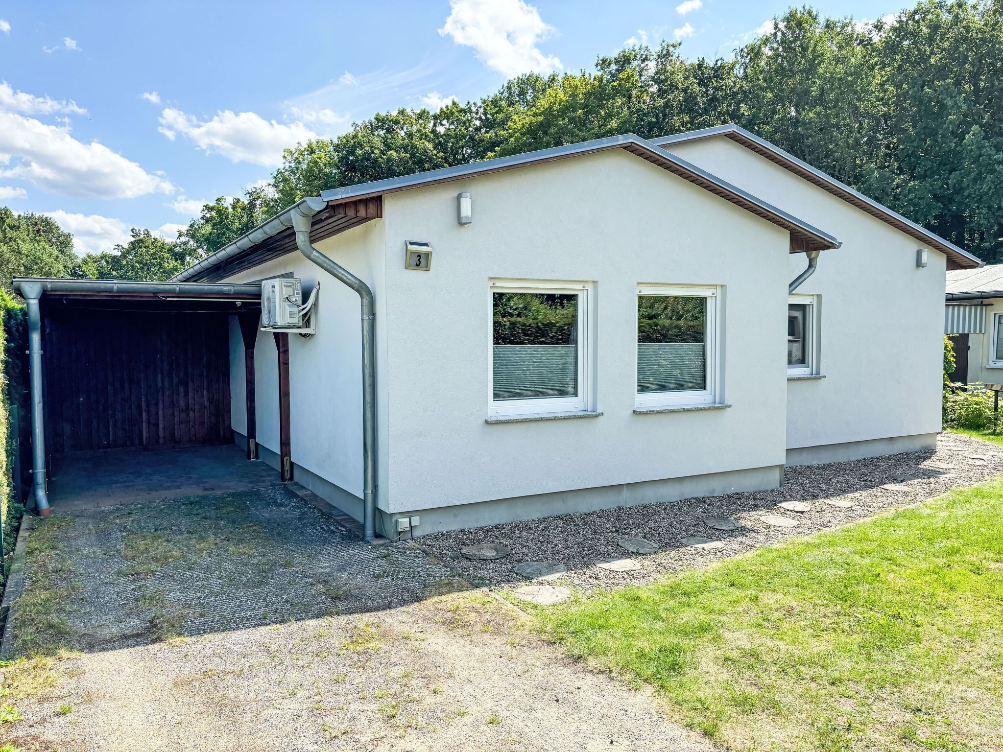 A single-story building with a covered garage, a small porch, and a gravel driveway.