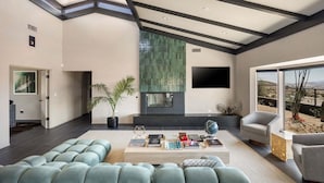 Een moderne woonkamer met een grote modulaire bank, een open haard, een flatscreen televisie en uitzicht op de woestijn.