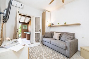 A modern living room with a grey sofa, a small table with a lamp, and a ceiling fan. - Il Vecchio Faro 19, Porto San Paolo, Italy (Porto San Paolo)