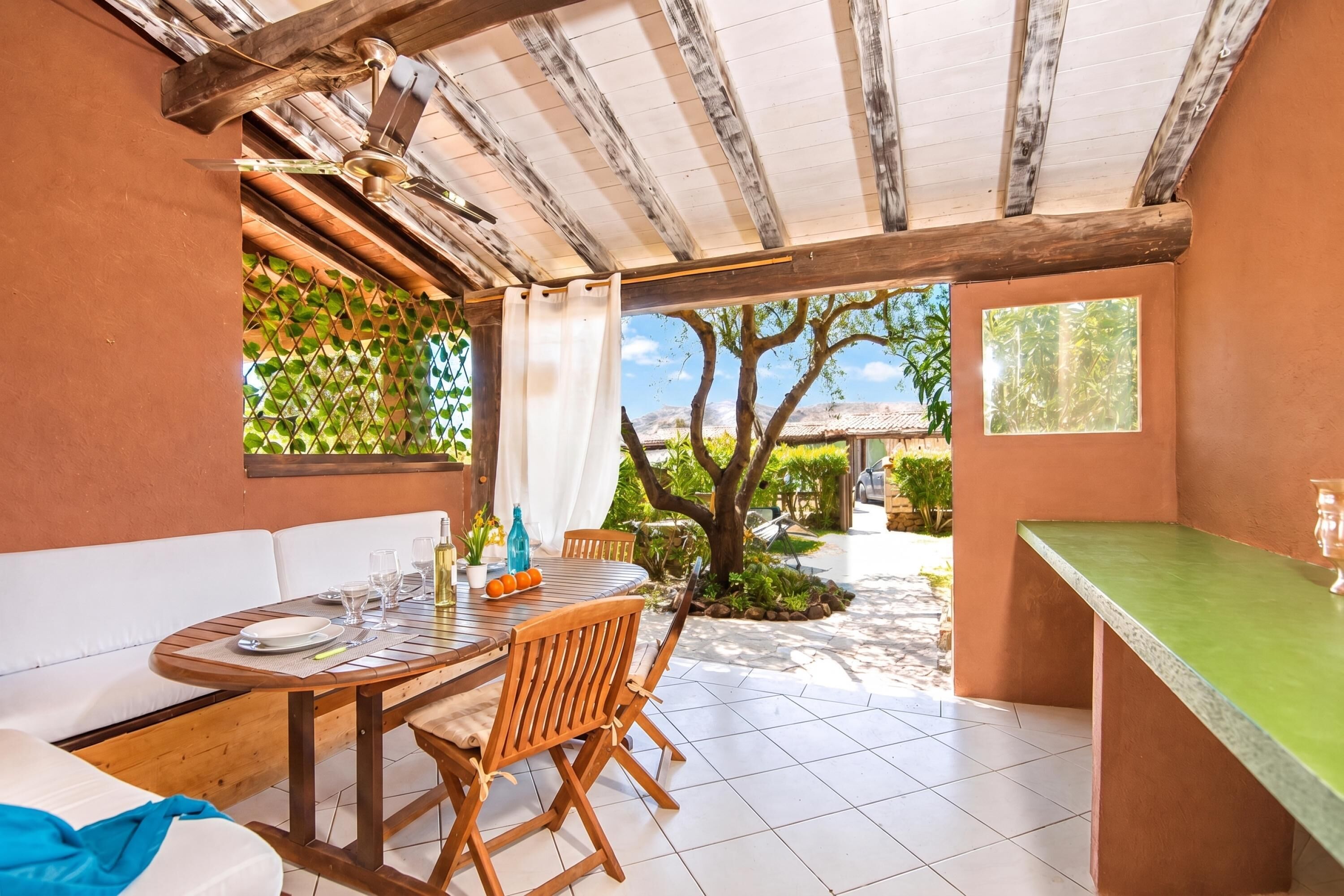 Un comedor con una mesa preparada para cuatro personas, techo de madera y vistas a un jardín.